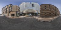 an intersection of two buildings with a bus parked on the other side of it as seen in a fisheye lens