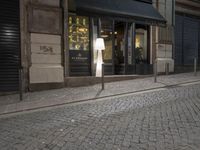 a woman walking down the street at night time, with her suitcase on the sidewalk