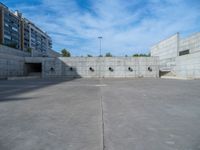 the empty parking lot in front of a wall with apartment buildings on it and a skateboarder on a ramp