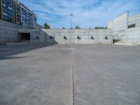 the empty parking lot in front of a wall with apartment buildings on it and a skateboarder on a ramp