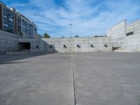 the empty parking lot in front of a wall with apartment buildings on it and a skateboarder on a ramp