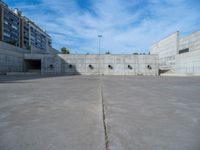 the empty parking lot in front of a wall with apartment buildings on it and a skateboarder on a ramp