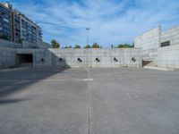 the empty parking lot in front of a wall with apartment buildings on it and a skateboarder on a ramp