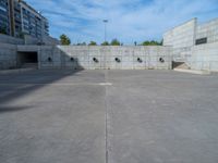 the empty parking lot in front of a wall with apartment buildings on it and a skateboarder on a ramp