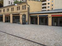 an empty street with small stores in the center of buildings in a european city by day