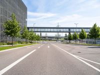 an empty road with a foot bridge and some bushes outside of the building on a sunny day