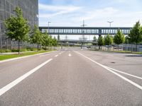 an empty road with a foot bridge and some bushes outside of the building on a sunny day