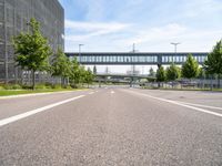 an empty road with a foot bridge and some bushes outside of the building on a sunny day