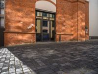 a sidewalk with chairs next to the brick building on the side, some have stairs and some buildings in the background