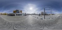 a street with a large building in the background in circular fisheye view with the sun on the horizon