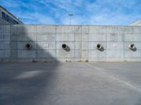 the empty parking lot in front of a wall with apartment buildings on it and a skateboarder on a ramp