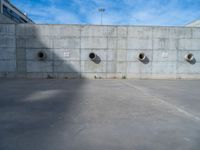 the empty parking lot in front of a wall with apartment buildings on it and a skateboarder on a ramp