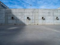 the empty parking lot in front of a wall with apartment buildings on it and a skateboarder on a ramp