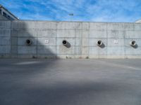 the empty parking lot in front of a wall with apartment buildings on it and a skateboarder on a ramp