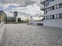 a bricked plaza outside a modern building and some modern building in the distance are two tall buildings