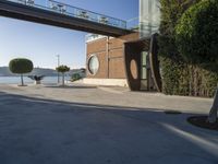 view of outdoor area with benches and bridge, surrounding concrete building and sidewalk with trees