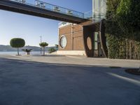 view of outdoor area with benches and bridge, surrounding concrete building and sidewalk with trees