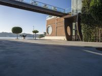 view of outdoor area with benches and bridge, surrounding concrete building and sidewalk with trees