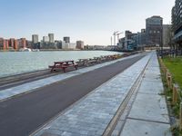 a paved path on a river side by the city and two empty benches lined up against a line