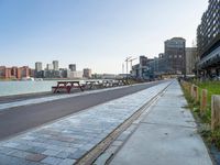 a paved path on a river side by the city and two empty benches lined up against a line