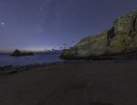 a star filled night sky over some rocks and water on the shore with rocks in foreground