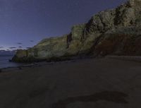 a star filled night sky over some rocks and water on the shore with rocks in foreground