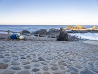 the beach has a stone walkway and several boats sitting on it, beside rocks, sand and water