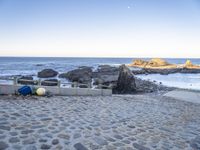 the beach has a stone walkway and several boats sitting on it, beside rocks, sand and water