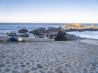 the beach has a stone walkway and several boats sitting on it, beside rocks, sand and water