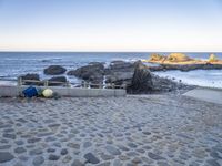 the beach has a stone walkway and several boats sitting on it, beside rocks, sand and water