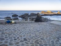 the beach has a stone walkway and several boats sitting on it, beside rocks, sand and water