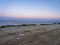 a beach at twilight with a sign on the side of road that warns to not go where