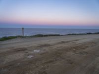 a beach at twilight with a sign on the side of road that warns to not go where