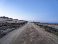 dirt road leading to the beach in open area with ocean in background and blue sky