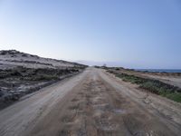 dirt road leading to the beach in open area with ocean in background and blue sky