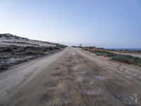 dirt road leading to the beach in open area with ocean in background and blue sky