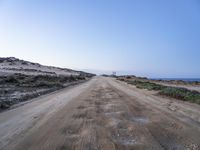 dirt road leading to the beach in open area with ocean in background and blue sky