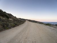 an empty dirt road in the desert, with some rocks on either side of the road, along with mountains in the distance