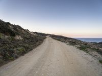 an empty dirt road in the desert, with some rocks on either side of the road, along with mountains in the distance