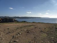 a beach with a field and water on it's side and rocks, grass, and grass