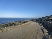 a deserted dirt road on the edge of a cliff with sea and cliffs in background