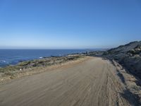 a deserted dirt road on the edge of a cliff with sea and cliffs in background