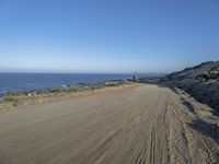 a deserted dirt road on the edge of a cliff with sea and cliffs in background