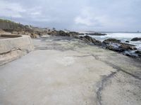 a sandy shore near a beach next to the ocean waves roll in on the rocks