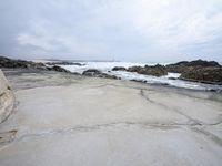 a sandy shore near a beach next to the ocean waves roll in on the rocks