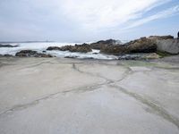 a sandy shore near a beach next to the ocean waves roll in on the rocks