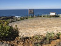 a stone surface in front of a beach and a bench near the water on a sunny day