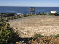 a stone surface in front of a beach and a bench near the water on a sunny day