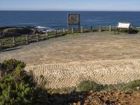 a stone surface in front of a beach and a bench near the water on a sunny day