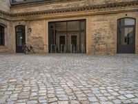 the sidewalk has a bike in front of the entrance to the building with the bicycle chained to the wall